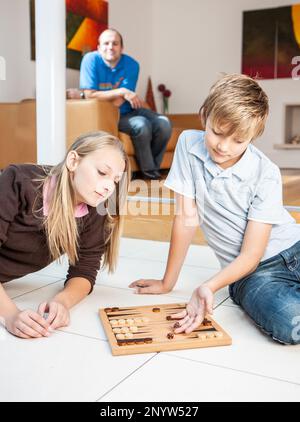 Vie familiale, rivalité entre frères et sœurs. Un frère et une sœur ont été enbrosés dans un jeu de backgammon à la maison tandis que le père regarde. À partir d'une série d'images associées. Banque D'Images