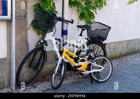 Vélos pour adultes et enfants garés près du mur du bâtiment. Casque jaune attaché à un vélo. Banque D'Images