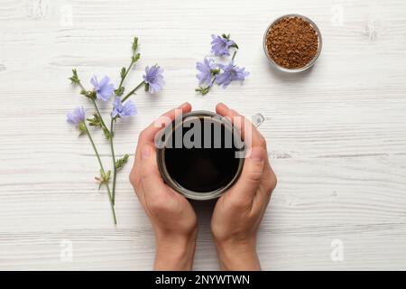 Femme tenant une tasse de délicieux chicorée à la table en bois blanc, vue de dessus Banque D'Images