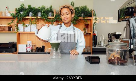 Une femme Barista verse de l'eau de la bouilloire à un filtre au comptoir Banque D'Images