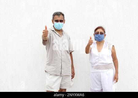 Couple Latino plus ancien avec des masques protecteurs sur fond de mur blanc, nouveau normal Covid-19 Banque D'Images