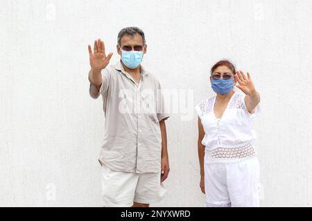 Couple Latino plus ancien avec des masques protecteurs sur fond de mur blanc, nouveau normal Covid-19 Banque D'Images