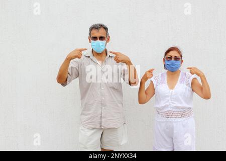 Couple Latino plus ancien avec des masques protecteurs sur fond de mur blanc, nouveau normal Covid-19 Banque D'Images