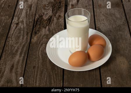 un verre de lait et trois œufs de poulet sur une table Banque D'Images