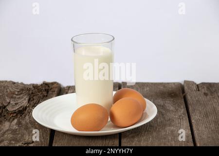 un verre de lait et trois œufs de poulet sur une table Banque D'Images