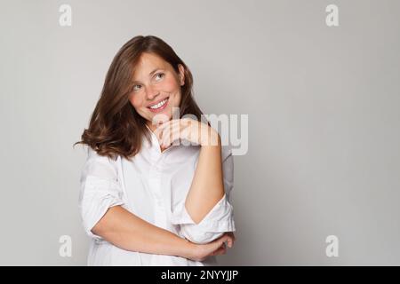 Bonne femme en chemise blanche regardant sur fond blanc de mur de studio. Banque D'Images