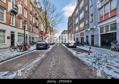 une rue enneigée avec des voitures garées et des vélos sur le trottoir devant un immeuble d'appartements, entouré de neige Banque D'Images