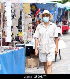Latino adulte plus âgé avec masque de protection et chapeau marchant sur plaza, nouveau normal Covid-19 Banque D'Images