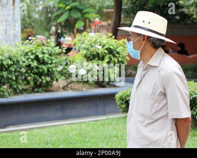 Latino adulte plus âgé avec masque de protection et chapeau marchant sur plaza, nouveau normal Covid-19 Banque D'Images