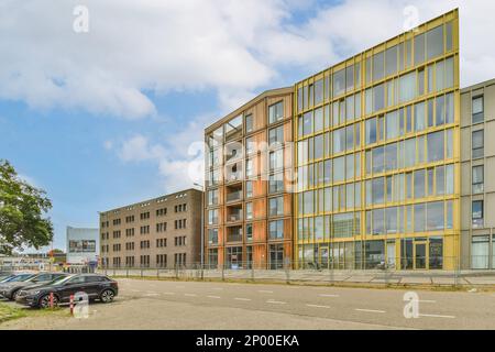 Amsterdam, pays-Bas - 10 avril 2021 : un parking devant un immeuble de bureaux avec des voitures garées dans la rue à côté et un ciel bleu rempli de nuages Banque D'Images