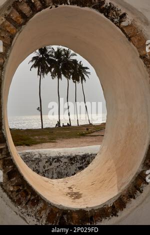 Vue sur les palmiers et la mer à travers une fenêtre en pierre au château d'Elmina, Elmina, Ghana Banque D'Images