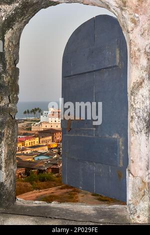 Vue sur les bâtiments et la mer à travers une fenêtre en pierre au château d'Elmina, Elmina, Ghana Banque D'Images