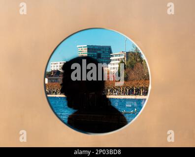 Zoug, Suisse - 31 décembre 2021: Une vue à travers l'ouverture ronde sur la promenade de Zoug en Suisse et une silhouette d'un homme passant par Banque D'Images