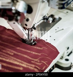 Gros plan des pièces de la machine à coudre avec un chiffon rouge foncé sur l'usine, l'aiguille et le fil, le processus de travail Banque D'Images