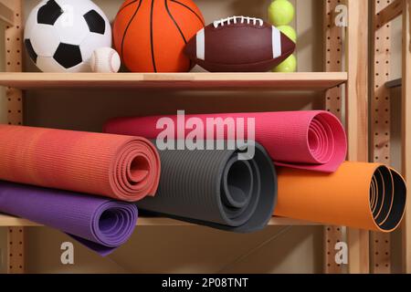 Différents ballons de sport et tapis de yoga sur le rack à l'intérieur Banque D'Images