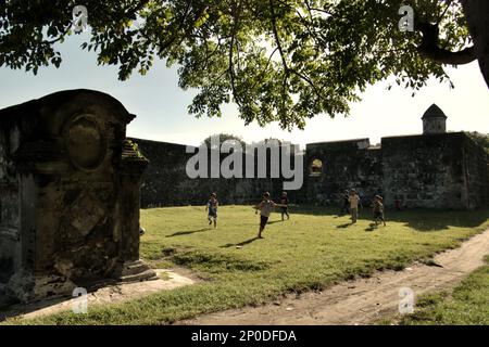 Les enfants jouent au football sur un terrain d'herbe près d'un cimetière européen et de fort Speelwijk, un fort hollandais construit sur le territoire de Banten Sultanat dans une région maintenant appelée Banten Lama (ancienne Banten) à Serang, Banten, Indonésie, sur cette photo prise en 2010. Une étude de terrain menée récemment par Nurikah et E. Rakhmat Jazuli (Faculté de droit, Université Sultan Ageng Tirtayasa, Banten) a révélé qu'il y avait de nombreuses violations contre le traitement des objets du patrimoine culturel dans la région. Les gens « mènent des activités sportives dans l'environnement des objets du patrimoine culturel, par exemple... Banque D'Images