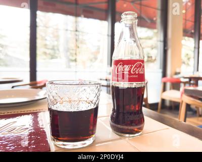 Erevan, Arménie, 28 février 2023: Photo de la boîte de Coca-Cola Classic bouteille de verre et tasse dans le restaurant. Bouteille de Coca-Cola et coca cola en verre. Banque D'Images