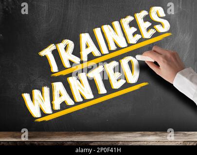 Close-up of hand holding morceau de craie contre tableau noir avec texte stagiaires voulait Banque D'Images