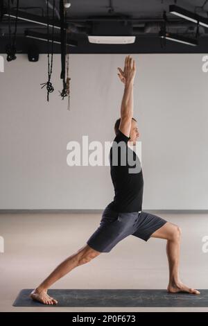 Un homme de construction athlétique fait du yoga dans la salle de gym sur un tapis. Banque D'Images