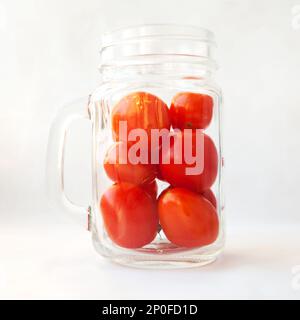 Les jus de tomates, de boire un verre de smoothie, concept. Tomates italiennes dans un pot transparent mug isolé sur blanc. De nombreux petits légumes rouges frais dans une tasse Banque D'Images