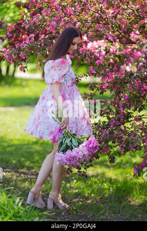 une fille dans une robe rose, debout avec un grand bouquet de pivoines, Banque D'Images