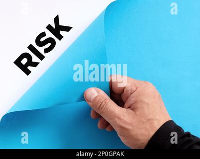Pour découvrir le concept de risques métier cachés. La main masculine ouvre le papier bleu et révèle le mot risque. Banque D'Images