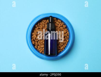 Bouteille en verre de teinture et nourriture sèche pour animaux dans un bol sur fond bleu clair, vue du dessus Banque D'Images