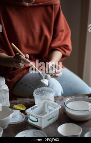 Ceramiciste femelle ou potier tenant le pinceau appliquant du glaçure sur des morceaux de céramique Banque D'Images