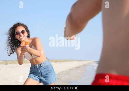 Couple avec des pistolets à eau s'amusant sur la plage Banque D'Images