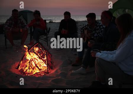 Groupe d'amis se rassemblant autour d'un feu de joie sur la plage le soir. Saison de camping Banque D'Images