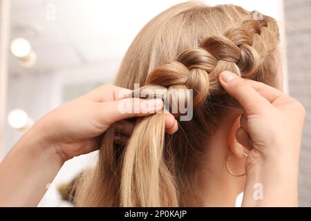 Styliste professionnelle braiant les cheveux du client dans le salon, en gros plan Banque D'Images