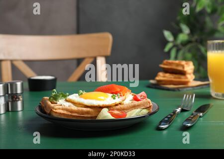 Gaufres belges délicieuses avec œufs frits, saumon, fromage à la crème et légumes servis sur une table en bois vert Banque D'Images