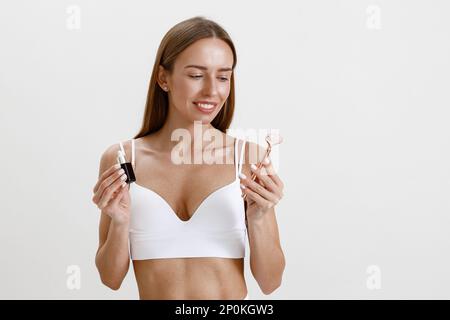La femme tient un flacon avec du sérum ou de l'huile hydratant pour les cosmétiques et un rouleau pour le visage sur fond de studio Banque D'Images
