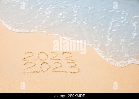 Dates écrites sur une plage de sable. 2022 lavé par la vague de mer comme nouvelle année 2023 à venir Banque D'Images