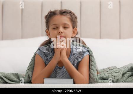 Petite fille mignonne priant sur la Bible dans la chambre Banque D'Images