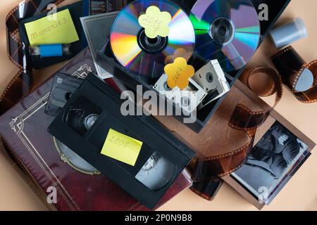 Vue de dessus sur différents périphériques de stockage avec archive de famille. Cassette VHS, disque optique, film en rouleau pour appareil photo, poignée de commande, disque dur usb, album de famille. Banque D'Images