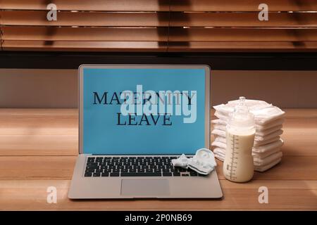 Accessoires de soins pour bébés et ordinateur portable avec texte congé de maternité sur table en bois à l'intérieur Banque D'Images