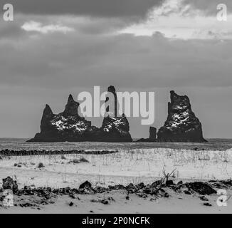 Pierres noires de la plage de Reynisfjara à l'horizon de la plage de sable noir sous un ciel spectaculaire et un sol entièrement recouvert de neige en noir et blanc Banque D'Images