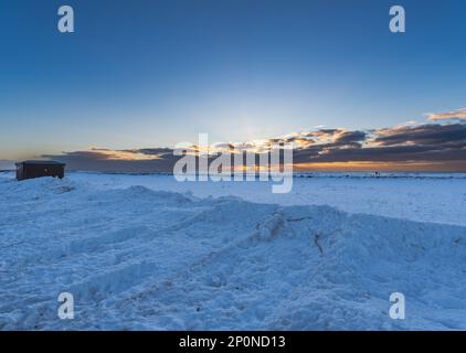 Paysage de la plage Plage sable noir plage complètement couverte de neige avec lumière dorée de l'aube sous les nuages et deux hommes marchant sur l'horizontale Banque D'Images