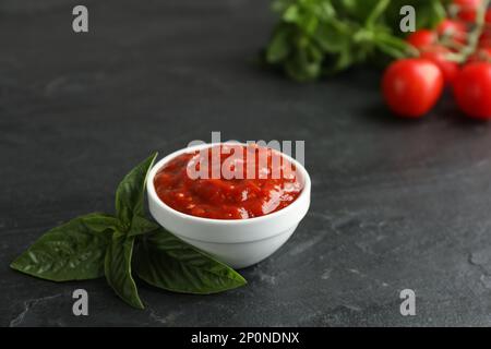 Délicieuse sauce adjika dans un bol avec basilic sur une table noire Banque D'Images