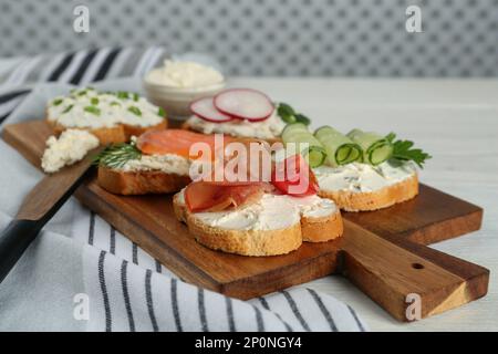 Pain grillé avec fromage à la crème et différentes garnitures sur table en bois blanc Banque D'Images