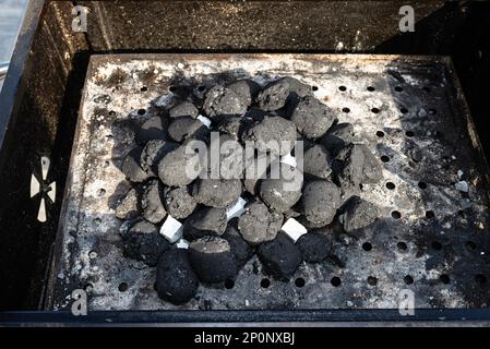 Éclairage d'un gril maison avec charbon de bois et blanc pour le gril, debout dans le jardin de la maison. Banque D'Images