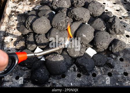 L'éclairage d'un gril maison avec charbon de bois et blanc pour l'allumage du gril, debout dans le jardin de la maison, à l'aide d'un barbecue plus léger. Banque D'Images