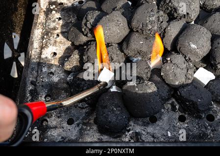 L'éclairage d'un gril maison avec charbon de bois et blanc pour l'allumage du gril, debout dans le jardin de la maison, à l'aide d'un barbecue plus léger. Banque D'Images