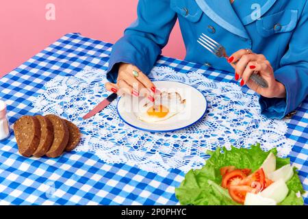 Vue de dessus image de la main femelle mettant la cigarette dans le jaune d'œuf sur les œufs frits à la nappe rétro à carreaux. Photographie d'art pop. Banque D'Images