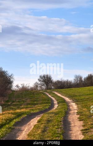 Route rurale de terre qui traverse les hautes terres de campagne à la frontière d'un champ agricole sous ciel bleu et nuages. Magnifique paysage de printemps Banque D'Images