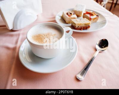 Le petit-déjeuner au café est servi dans une tasse blanche avec cappuccino et assiette de pâtisseries. Desserts savoureux et café chaud. Banque D'Images