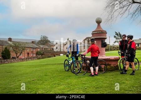 Cyclistes par la vieille fontaine d'eau sur le vert du village, avec Dufton Pike derrière, Dufton, Eden Valley, Cumbria. Fontaine d'eau construite par London Lead Co. Banque D'Images