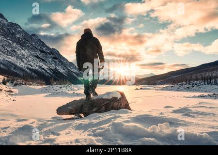 Vue arrière d'un jeune aventurier en solo debout sur un lac enneigé avec lever du soleil au-dessus du lac Medicine le matin en hiver au parc national Jasper, en Alberta Banque D'Images