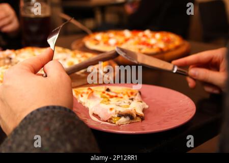 Pizza avec couteau et fourchette. Main mâle. La personne de Defocus coupe la pizza dans le café. Jeune homme affamé avec couteau et fourchette de couper et de manger de la pizza dans le café Banque D'Images